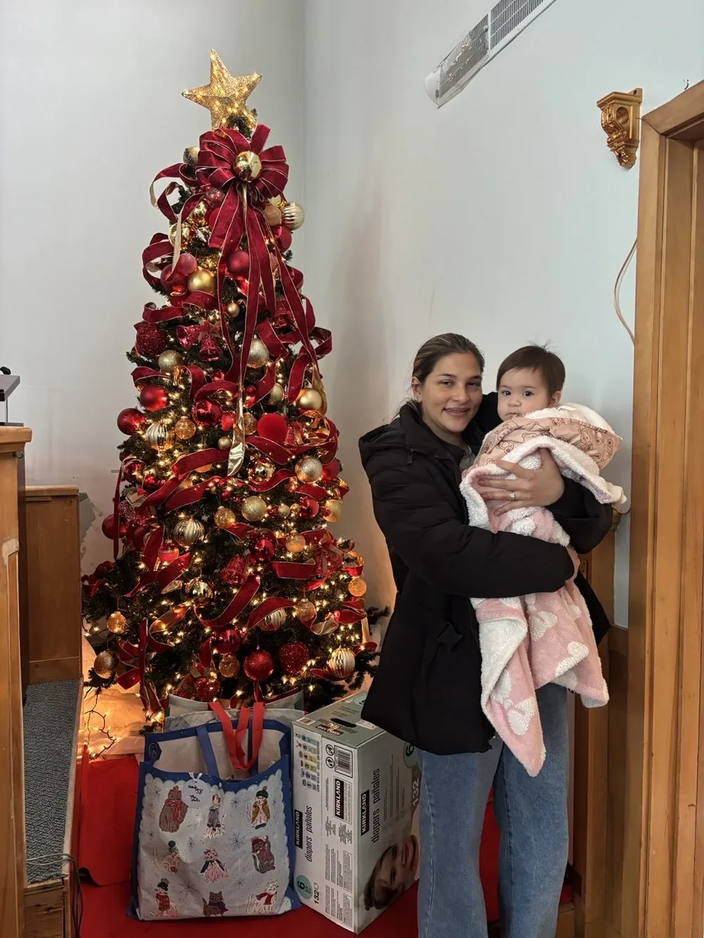 A woman holding a young child beside the Christmas tree.